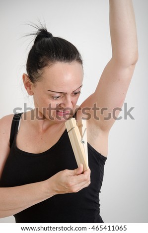 Body Odor, woman with a disgusted look on her face smelling her armpit and putting a large wooden peg on her nose.