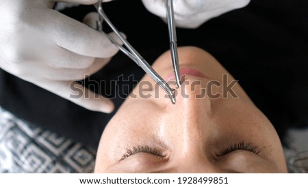 Body piercing process. Professional piercer in the disposable gloves sets nose ring properly 
