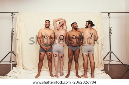 Body positive men wearing underwear in a studio. Four happy men standing with the letters that read’ ’BODY POSITIVITY” written on their bodies. Self-confident young men embracing their natural bodies.