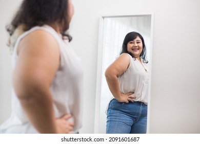 Body positive plus size female clothing. Body positive plus size woman happily and is proud of herself looking at mirror at home. Try wearing clothes that measure the size.