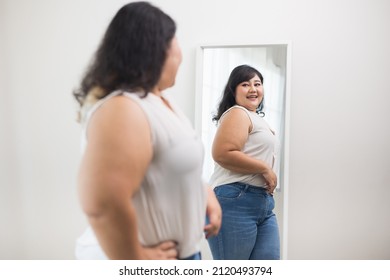 Body Positive Plus Size Female Clothing. Body Positive Plus Size Woman Happily And Is Proud Of Herself Looking At Mirror At Home. Try Wearing Clothes That Measure The Size.