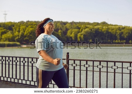 Body positive plus size woman jogging outdoors and having sport walking losing weight. Happy smiling fat girl having sport training in nature walking on the bridge along the river in the city park.