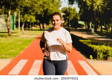 Body positive plus-size plump woman athlete jogging running in fitness outfit, losing weight while listening to music in stadium outdoors
