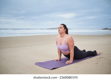 Body positive woman wearing sport clothes stretching in cobra pose on yoga mat - Powered by Shutterstock