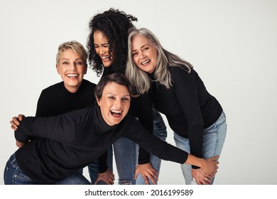 Body positive women of different ages celebrating their natural bodies in a studio. Four confident and happy women smiling cheerfully while wearing jeans against a white background.
