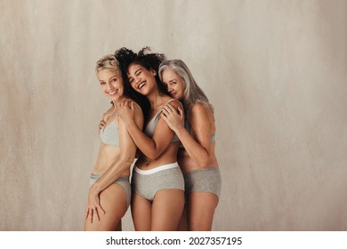 Body positive women of different ages embracing their natural bodies. Group of three happy women wearing underwear and smiling cheerfully. Women posing against a studio background.