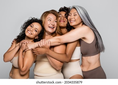 Körperpositive Frauen umarmten interethnische Freunde in Dessous einzeln auf Grau