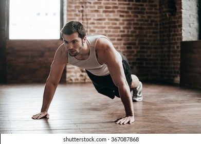 Body power. Confident muscled young man wearing sport wear and doing push-ups while exercising on the floor in loft interior - Shutterstock ID 367087868
