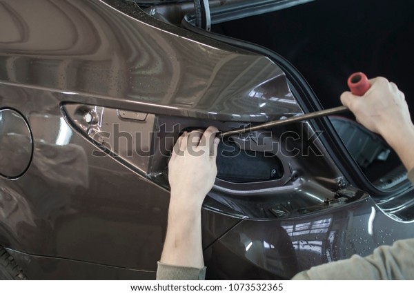 Body repair. The mechanic at the auto shop with\
tools to repair dents in car\
body