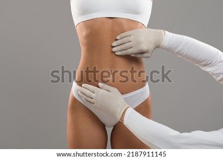 Body Sculpting Concept. Unrecognizable Young Female Getting Consultation At Plastic Surgery Clinic, Doctor In Gloves Examining Abdomen Area Of Woman In Underwear Before Treatment, Cropped