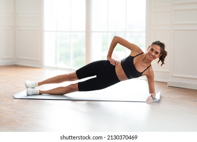 Body Shaping Concept. Smiling Fit Woman Standing In Side Plank Position On Yoga Mat Near Window At Home Or Fitness Studio, Looking Posing At Camera, Training Core And Abs Muscles, Free Copy Space - Powered by Shutterstock