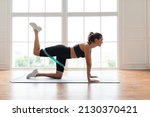 Body Shaping And Glutes Workout. Smiling Fit Woman Doing Donkey Kicks Exercise With Leg Raise On Yoga Mat Using Resistance Band, Training Butt Muscles And Hamstring. Profile Side View. Fitness Concept