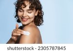 Body skin care. Smiling woman applying body cream portrait. Beautiful happy girl model with cosmetic moisturizing lotion on perfect hydrated soft skin on shoulder at studio, blue background.