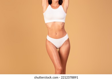 Body Slimming. Unrecognizable Young Lady With Slim Sporty Figure In White Underwear, Cropped Shot Of Woman Torso With Flat Abdomen Isolated Over Beige Studio Background