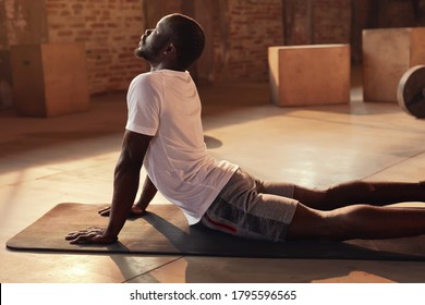 Body stretch. Fit man stretching back, doing yoga workout at gym. Black male athlete doing back extension stretch exercise lying on mat indoors - Powered by Shutterstock