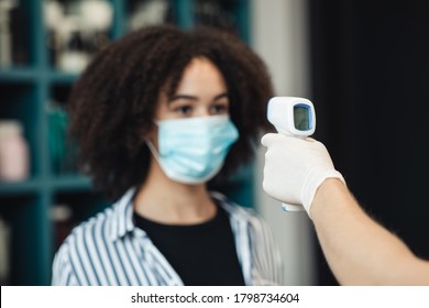 Body temperature check. Young black woman in medical mask getting thermal screening with contactless thermometer, close up - Powered by Shutterstock