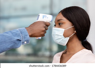 Body Temperature Control. Security Guard Using Digital Medical Electronic Thermometer For Black Woman Passenger In Airport Due To COVID-19, Closeup