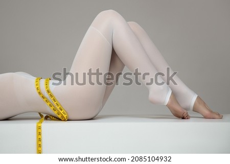 body of a woman in a white suit for LPG massage holds a centimeter in her hands. Anti-cellulite body care concept. Gray background