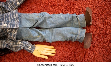 body of a wooden puppet with legs and arms dressed in cloth of jeans, and the boots and hands of painted wood, lying on a red carpet  - Shutterstock ID 2258184325