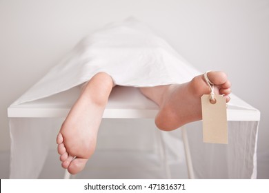 Body Of A Young Boy On A Mortuary Slab With His Bare Feet Sticking From Under The Sheet Covering Him With A Blank Tag Hanging From The Toe For Identification