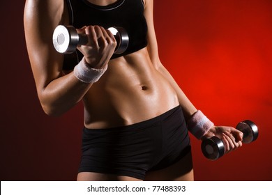 Body Of A Young Fit Woman Lifting Dumbell. Shot In Studio On A Red Background.