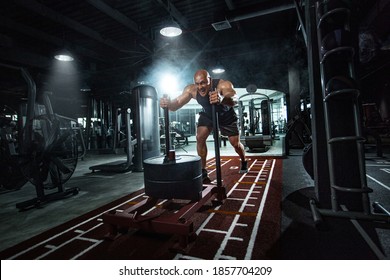 Bodybuilder athlete working out in the gym. Strong and fit man training with crossfit sled. Sport and fitness motivation. Individual sports recreation.