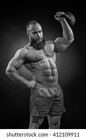 Bodybuilder with a beard lifts a heavy kettlebell. Black and white portrait of a strongman.