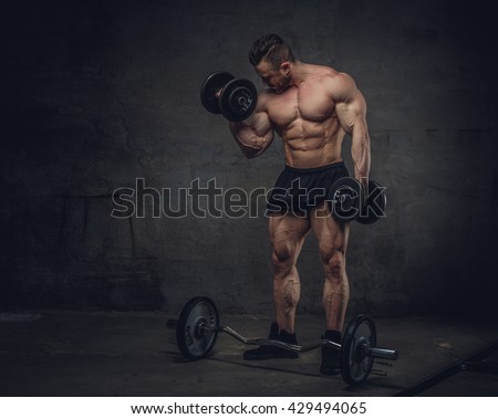 Bodybuilder doing biceps workouts on grey background in studio.