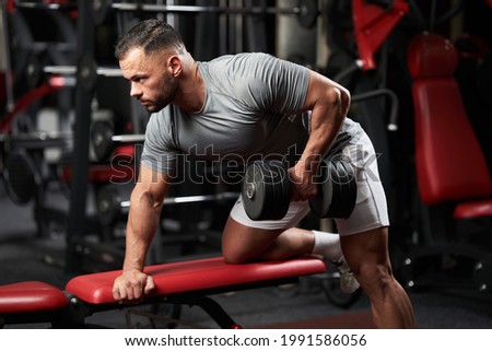 Bodybuilder doing dumbbell row for back workout on a bench in the fitness gym