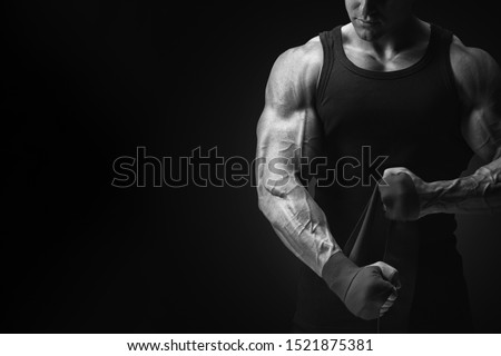 Bodybuilder fitness lifestyle concept Croped black and white shot on black background Man is wrapping hands with boxing wraps isolated Strong hands and fist, ready for training and active exercise
