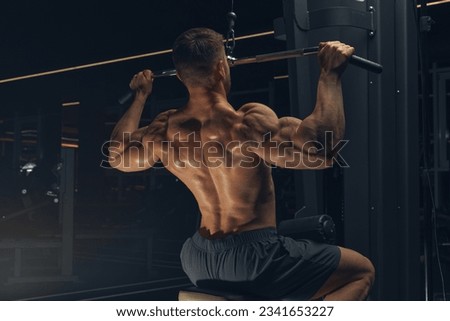 Bodybuilder in gym. Muscular man working out in gym, doing exercise back lat pulldown. Strong male rear view.