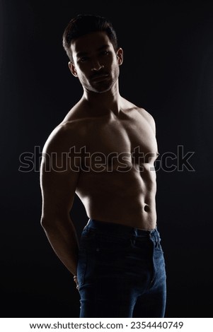 Bodybuilder man, topless and muscle in studio for wellness, healthy body and black background. Young guy, fitness and silhouette in jeans, portrait and strong for fashion, shadow or shirtless for art