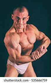 Bodybuilder posing in different poses demonstrating their muscles. Failure on a dark background. Male showing muscles straining. Beautiful muscular body athlete.