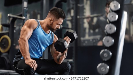Bodybuilder pumping his biceps with dumbbell in gym, empty space