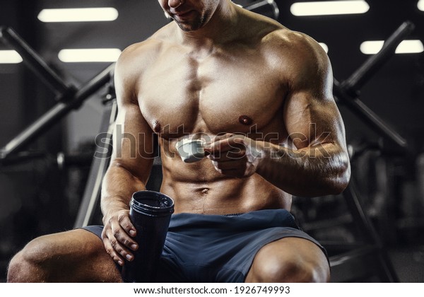 Bodybuilder strong athletic rough man with protein\
powder after workout workout fitness and bodybuilding healthy\
concept background - muscular fitness men doing exercises in gym\
naked torso