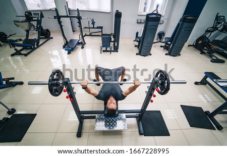 Bodybuilder trainer man doing bench press workout in gym. Photo from the top. Strong abs. Health life sport concept.