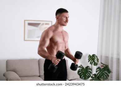 Bodybuilder training at home, doing hammer bicep curls with dumbbells. Young man performing physical exercises in his living room. Close up, copy space, background.