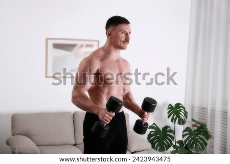 Bodybuilder training at home, doing hammer bicep curls with dumbbells. Young man performing physical exercises in his living room. Close up, copy space, background.