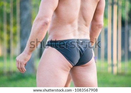 Bodybuilder wearing black swimming trunks on the beach.