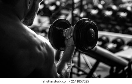 Bodybuilder working out with dumbbell weights at the gym. Black and white.