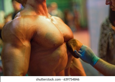 Bodybuilding Competition Backstage: Contestant Being Oiled And Fake Tan Applied To Skin. Selective Focus.