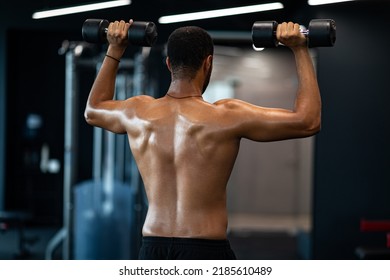 Bodybuilding Concept. Rear View Of Muscular Black Man Working Out With Dumbbells, Unrecognizable Young African American Male Athlete With Naked Torso Training With Light Weights At Modern Gym