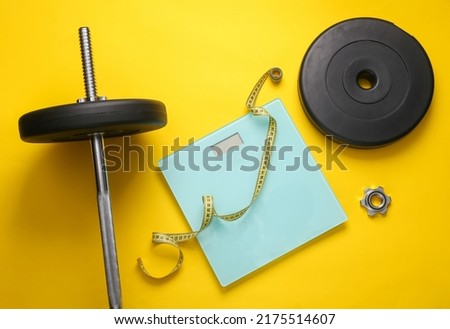 Bodybuilding and fitness. Losing weight or gaining muscle mass. Barbell with a measuring tape and scales on a yellow background. Top view. Flat lay