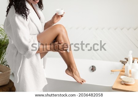 Bodycare. Cropped Shot Of Black Lady Moisturizing Smooth Legs With Cream Moisturizer In Modern Bathroom Indoor. Unrecognizable Female Applying Body Lotion Caring For Skin