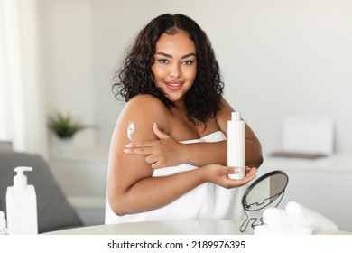 Bodycare And Skin Nutrition. Happy African American Plus Size Lady Using Body Lotion, Holding Bottle, Doing Daily Morning Routine, Pampering Herself After Bath