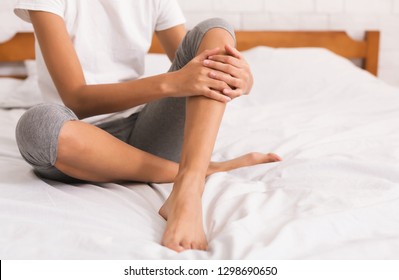 Bodycare. Woman With Bare Legs Sitting On Bed At Home, Crop, Copy Space