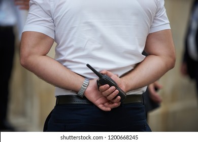 Bodyguard Holding Portable Radio Transceiver In Hand. Security Guard Holding Walkie Talkie In Hands Behind Back