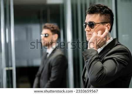 bodyguard service, private security, professional guards in suits and sunglasses standing in hotel lobby, handsome man with earpiece communicating with work partner, luxury hotel, vigilance Foto stock © 