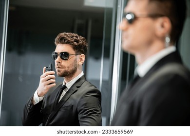 bodyguard service, private security, professionals in suit and sunglasses handsome man standing in hotel lobby and using walkie talkie near work partner, communication, luxury hotel, vigilance - Powered by Shutterstock