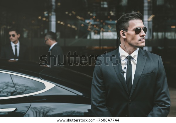 bodyguard standing at businessman car and reviewing\
territory 